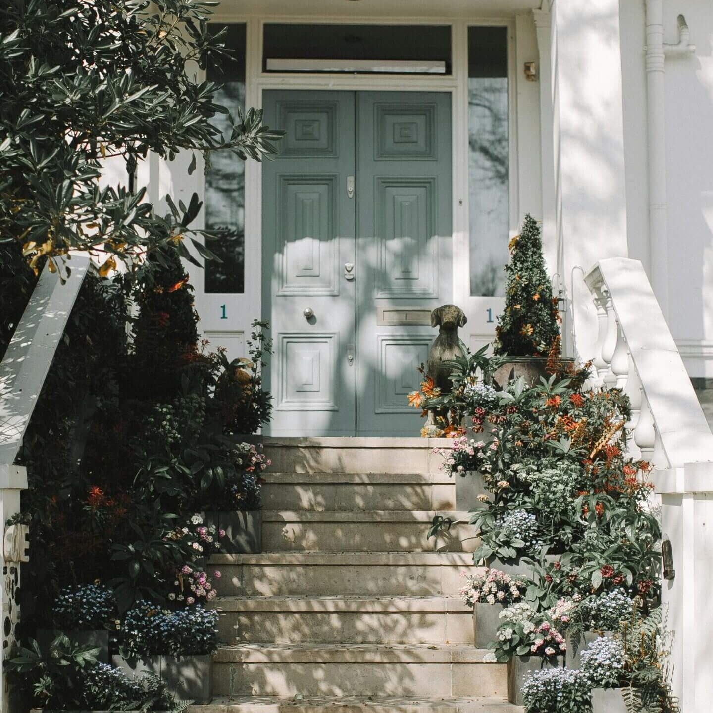 Stone steps leading to a pastel blue door surrounded by greenery.